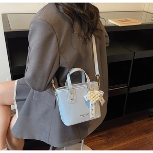 Detail of light blue leather bucket bag with white lace bow and pearl heart charm