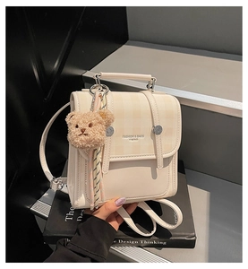 Close-up of cream mini backpack with yellow plaid flap and a cute brown plush bear charm