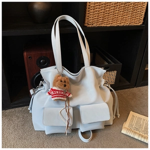 Detail of light blue PU leather tote bag with dual front pockets and teddy bear charm