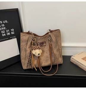 Close-up of brown textured leather tote with embossed bear motif and plush charm