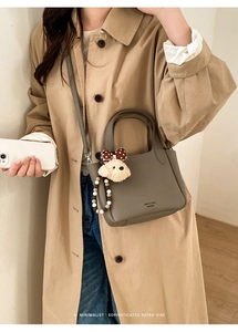 Detail of taupe lychee leather bucket bag with dog plush pendant on a trench coat model