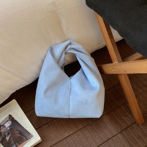 Close-up of light blue pleated cloud bag with unique knotted handle on minimalist background