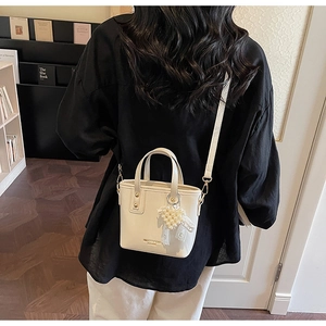 Detail view of a white bucket bag with pearl heart pendant and adjustable strap