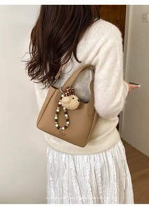 Detail of tan bucket bag featuring lychee grain leather and plush dog charm