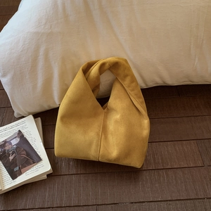 Close-up of bright yellow pleated cloud bag with unique knotted handle on wood floor