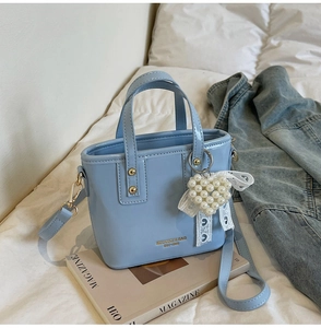 Detail of light blue glossy bucket bag with pearl heart charm and golden logo lettering