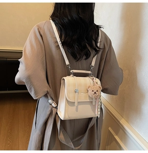 Detail of beige mini backpack with plaid flap and brown plush bear charm on back