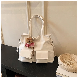 Detail of white leather tote bag featuring front flap pockets and cute brown bear charm