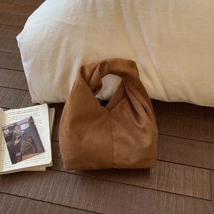 Close-up of caramel brown faux suede cloud bag with twisted handle on a wooden floor