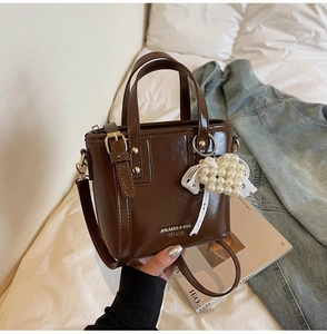 Close-up of dark brown bucket bag with pearl lace charm and golden hardware detail