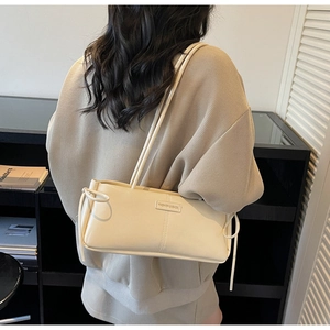 Detailed close-up of a beige glossy shoulder bag with minimalist stitching and slim straps