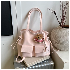 Detail of pink PU leather tote bag with front pockets and cute bear charm on a suitcase