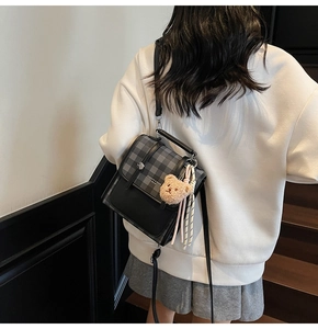 Detail of a retro plaid backpack with a cute bear charm on a model in a casual setting