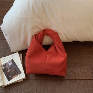 Detail view of the soft suede cloud bag with a unique knotted handle in brick red