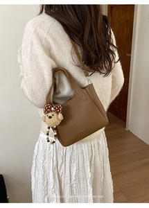 Detail of brown lychee texture leather handbag with cute plush bear and bow charm