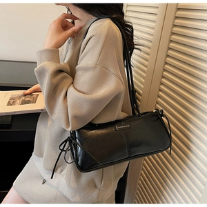 Detail of black glossy shoulder bag featuring delicate side ribbons and a fashion logo