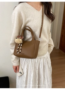 Close-up of brown litchi pattern leather handbag with plush puppy charm and brand logo