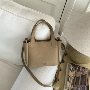 Detail shot of khaki lychee grain bucket bag on white sofa with vintage books