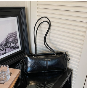 Detail view of the sleek black underarm bag featuring glossy wrinkled leather and logo plate