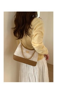 Sac sous le bras en toile beige avec chaîne dorée porté par un mannequin en tenue décontractée