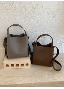 Detailed view of textured leather bucket bags in grey and brown on stone pedestals
