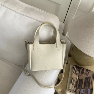 Close-up of cream lychee texture leather handbag with adjustable strap on white sofa