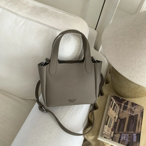Close-up of taupe litchi texture handbag with gold logo on a clean white sofa