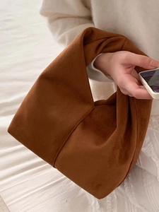 Dark brown suede cloud bag with minimalist knot handle held against a soft white background