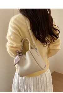 Detail einer cremefarbenen Beuteltasche mit Seidenschal am Griff für einen eleganten Look