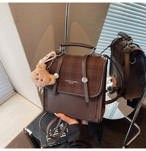 Detail view of brown vintage backpack with checkered flap and plush bear charm