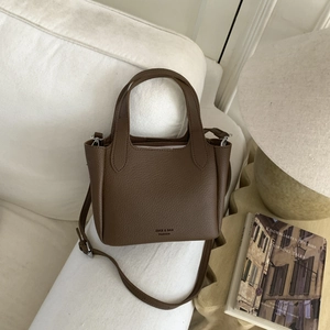 Detailed view of dark brown lychee grain texture and metal buckles on a small handbag