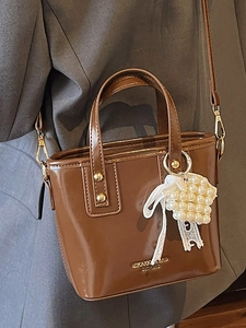 Brown glossy bucket bag with pearl charm and gold hardware shown on a shoulder