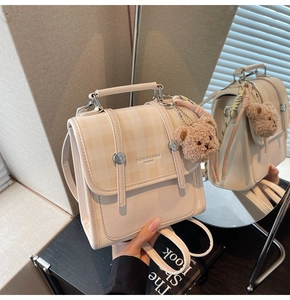 Detailed macro view of the checkered flap and plush bear charm on a beige backpack