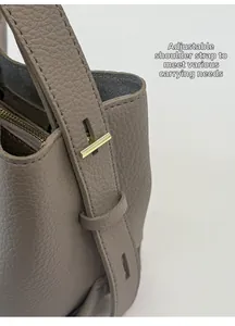 Close-up of golden T-buckle and adjustable shoulder strap on lychee leather bucket bag