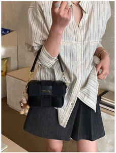 Detail of black woven shoulder bag with golden chain strap and a cute brown bear pendant