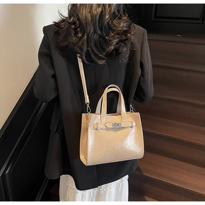 Detail view of a beige patent leather crossbody bag with silver clasp on a model