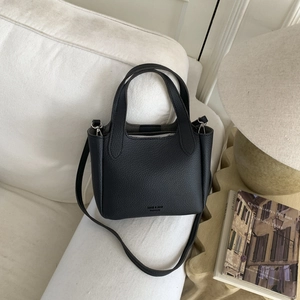 Detail of black lychee grain leather handbag on a sofa with adjustable shoulder strap