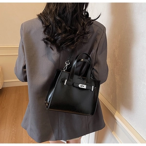 Detail view of the black glossy leather crossbody bag with silver buckle on a gray blazer