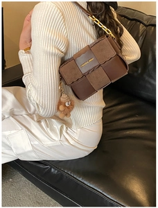 Detail of brown woven leather handbag with gold chain strap and teddy bear charm