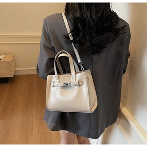 Detail shot of a beige shiny crossbody bag with silver hardware on a model's arm