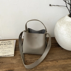 Minimalist taupe lychee leather bucket bag with top handle and wide shoulder strap