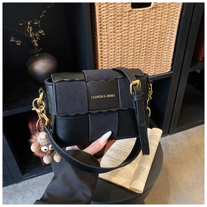 Close-up of woven black leather handbag with gold lettering and cute brown plush charm