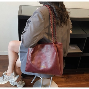 Détail d'un sac cabas tissé bordeaux avec poignée tressée et texte doré gaufré