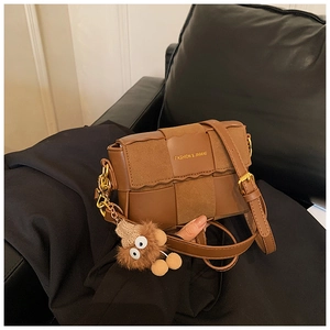 Detail of woven patchwork crossbody bag in caramel brown leather with funny monster charm