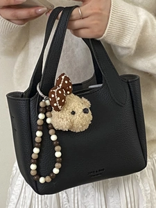 Black pebbled leather tote bag with bear charm and beaded strap held by a woman