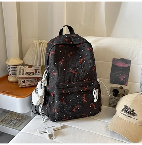 Detail of black backpack with white polka dots, red bows, and white plush charm on a sofa