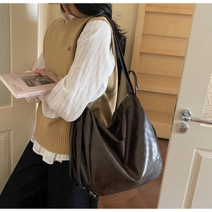 Deep brown oversized ruched tote bag in glossy PU leather worn by a model in warm light