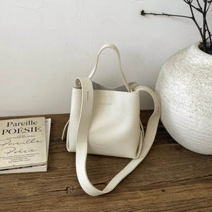 Minimalist white leather bucket bag with top handle and wide strap on a wooden bench