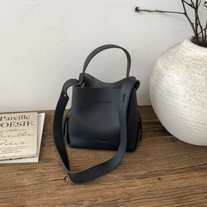 Detail of black pebbled leather bucket bag with top handle and wide shoulder strap