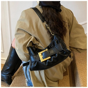 Detail of black pleated cloud bag featuring large gold buckle and mixed chain strap